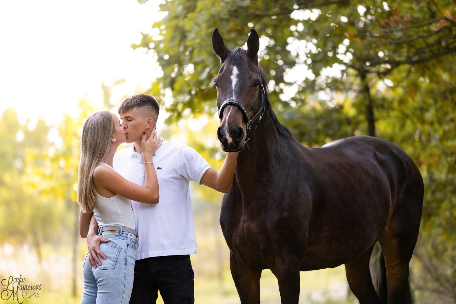 Couple sharing tender moment with dark horse in sunset nature setting.