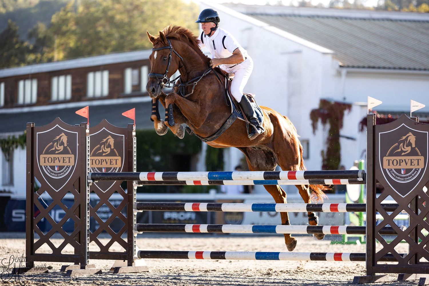 Equestrian rider on horseback clearing a jump during competition at an outdoor arena.