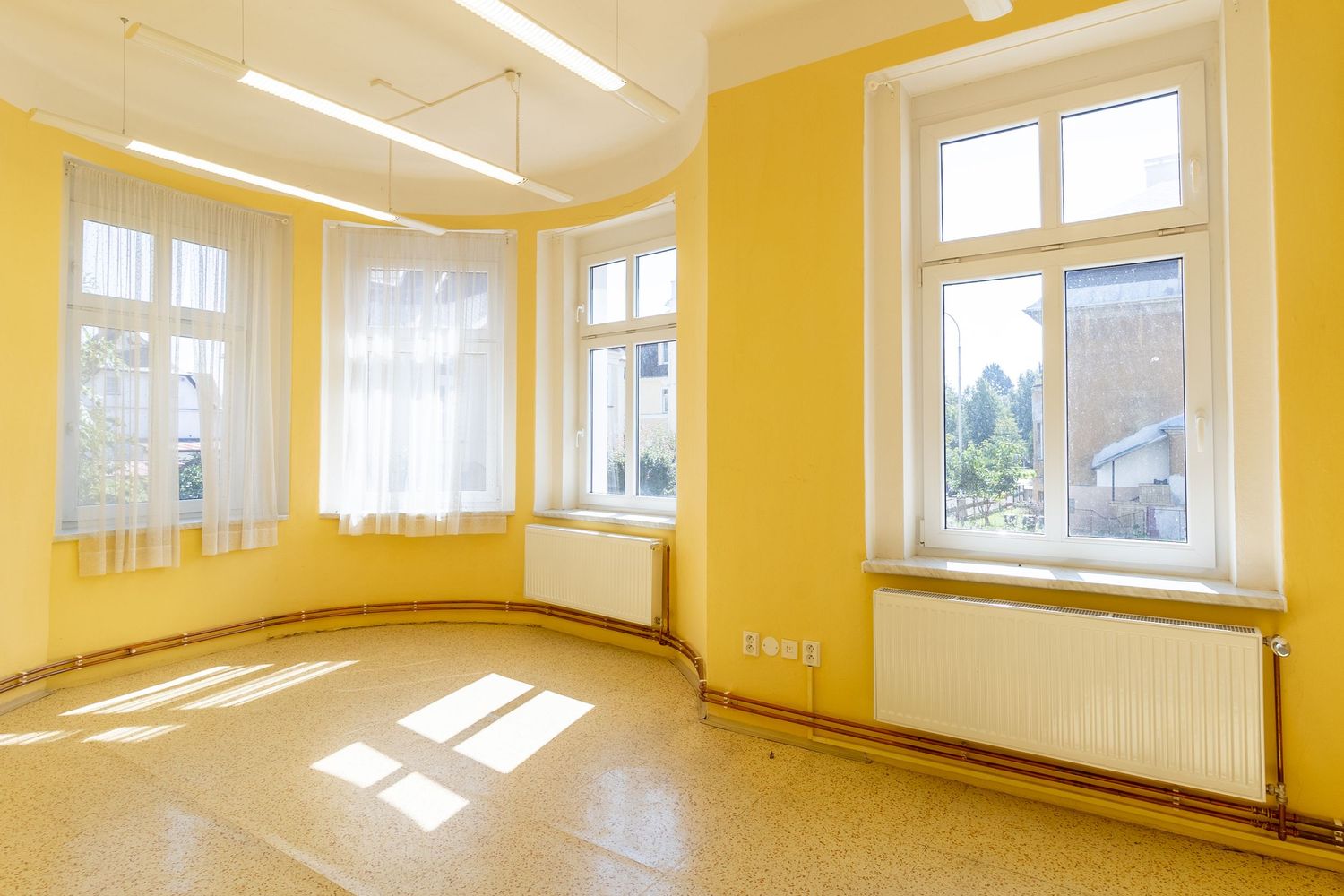 Bright empty room with yellow walls, white trim, and large windows letting in natural light.