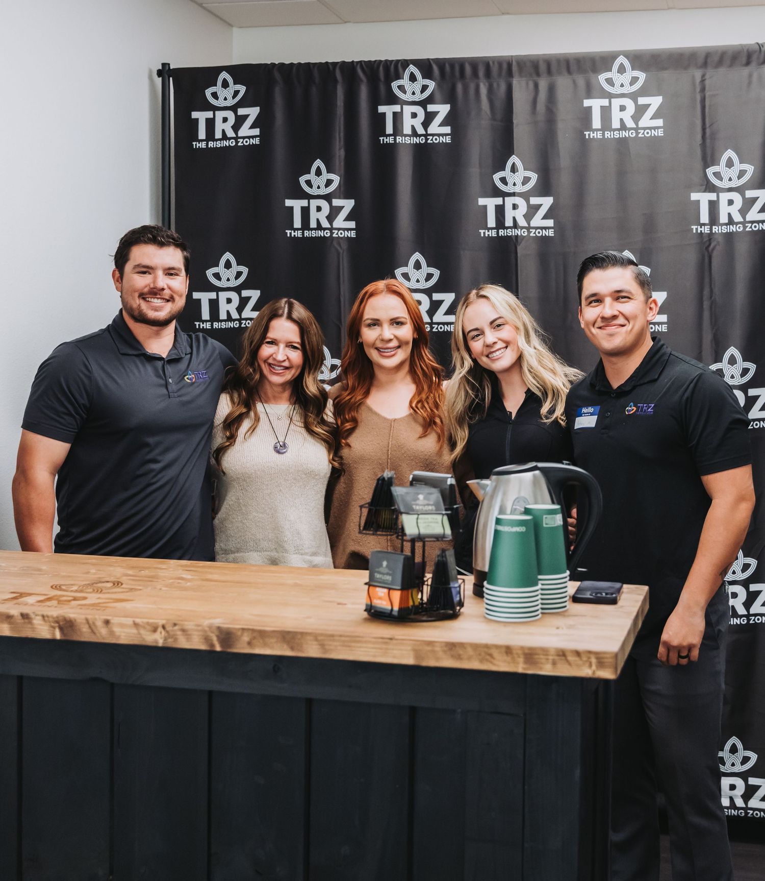 People gathered at a bar counter with TRZ branded backdrop for an event.