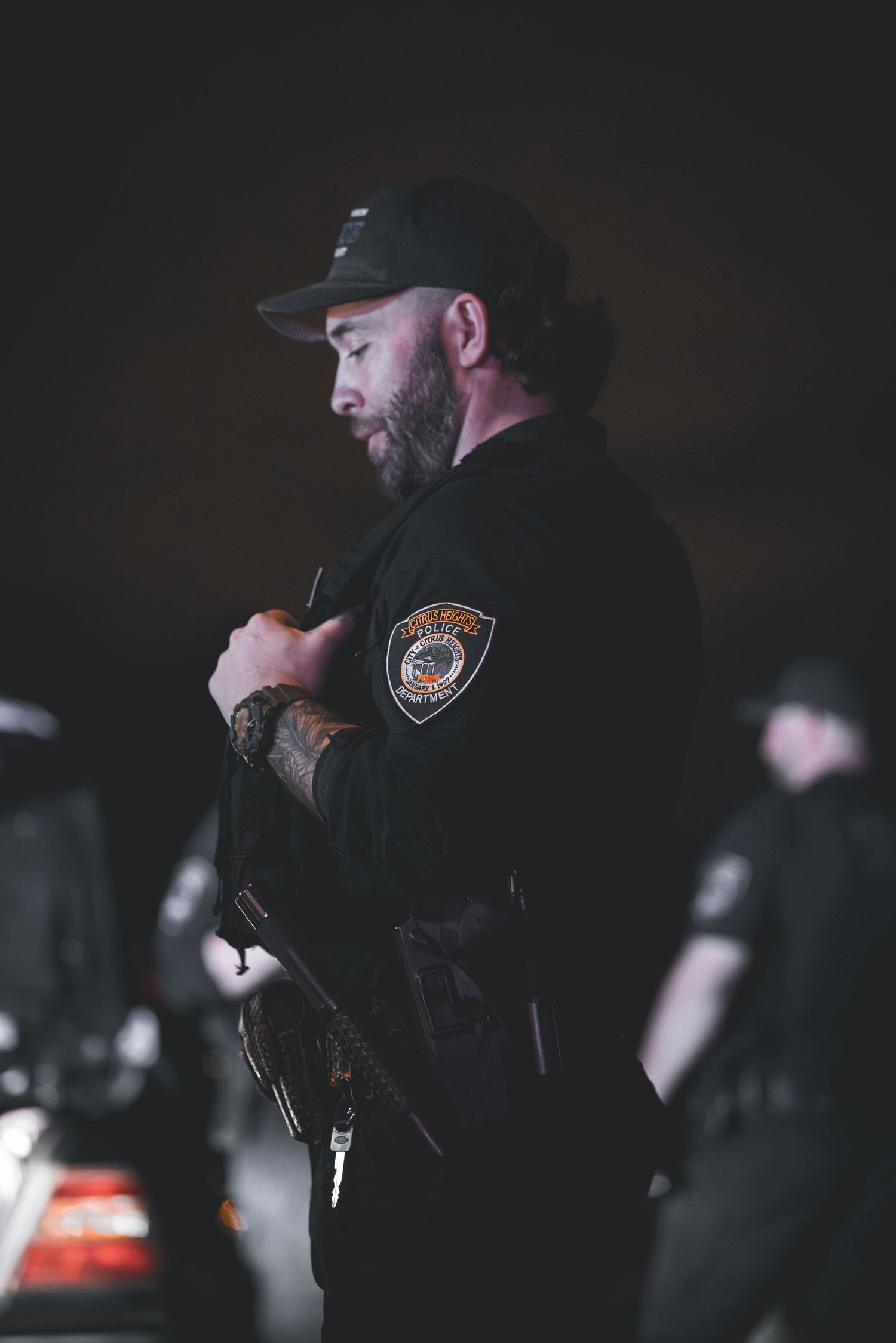 Police officer in dark uniform stands in low light conditions while using radio equipment at night.