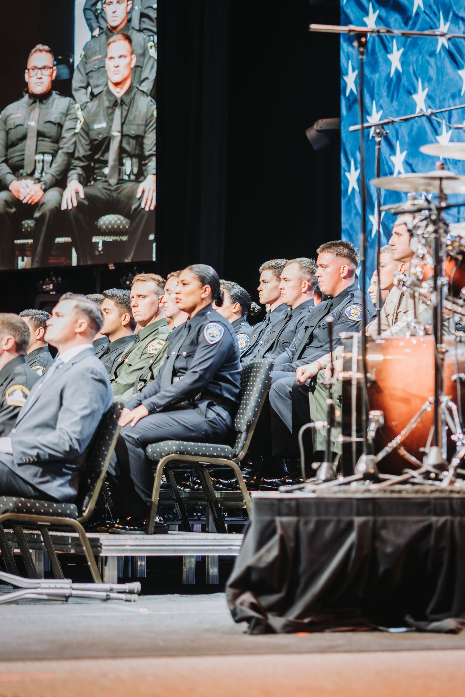 Law enforcement officials seated during a formal ceremony with American flag backdrop.