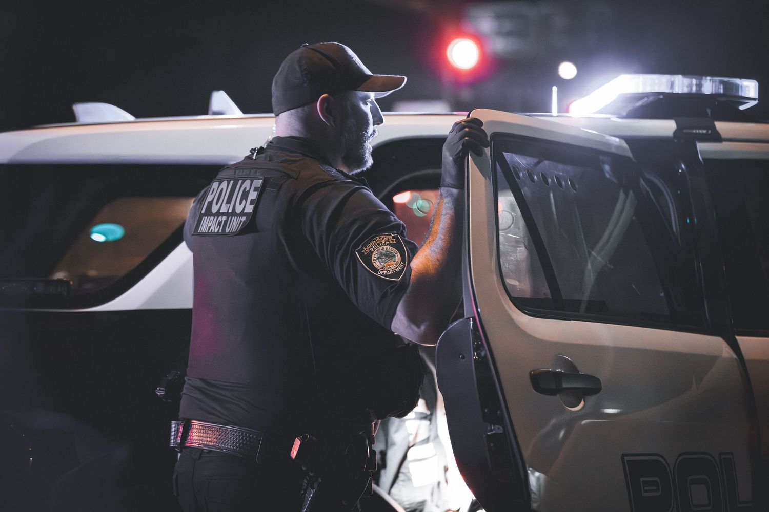 Police officers conduct a traffic stop at night with emergency lights illuminating the scene.