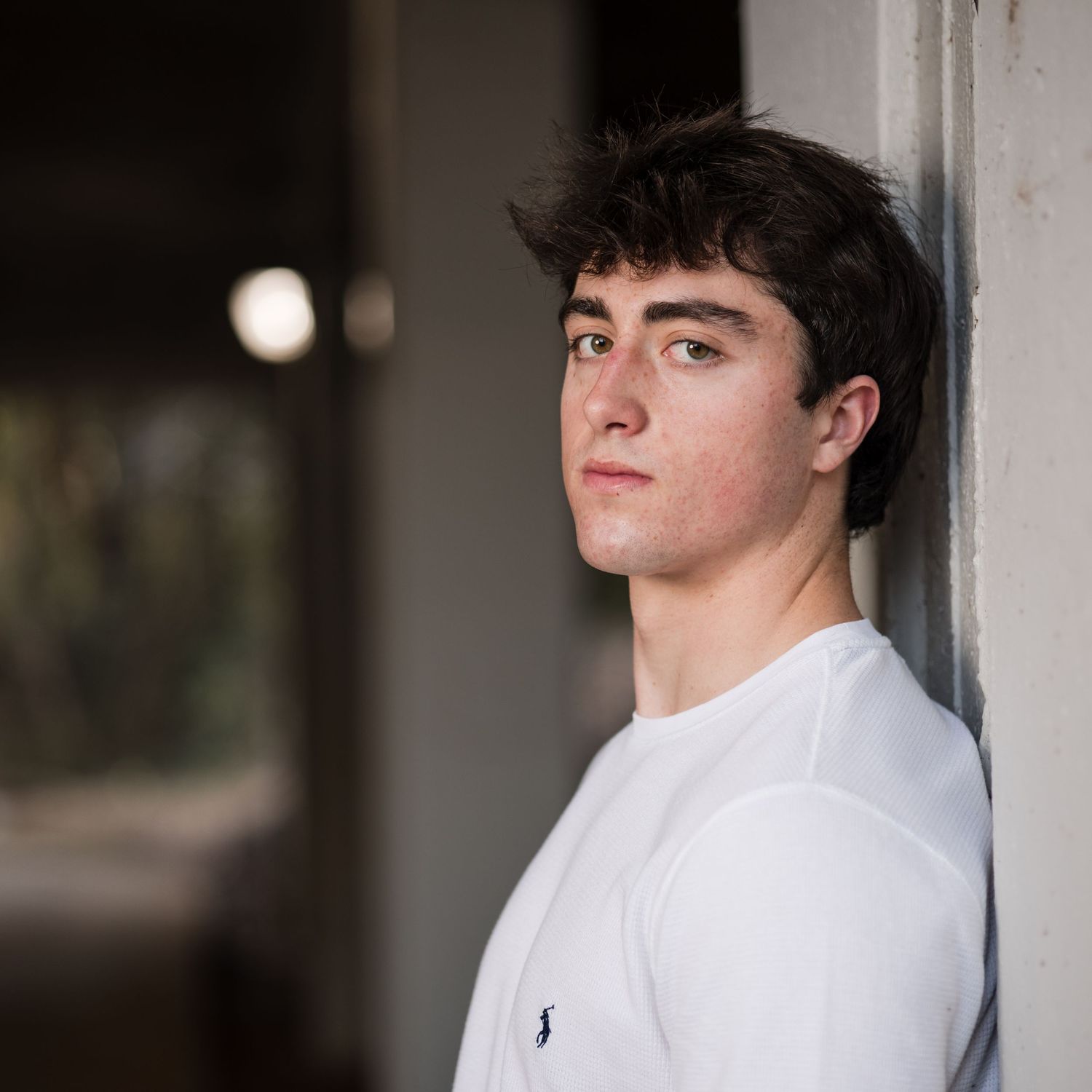 A person in a white button-down shirt looks to the side with a contemplative expression against a dark background.
