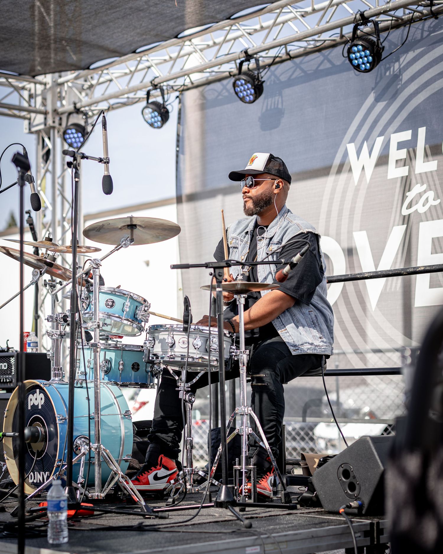Musicians performing on stage with drum kit and equipment under professional lighting setup.
