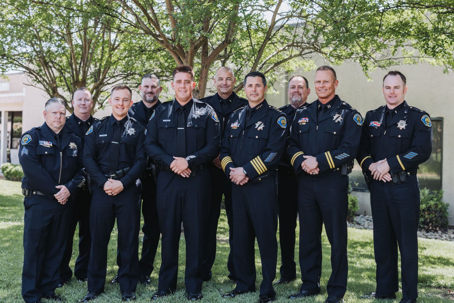 Group of uniformed officers standing in formation outdoors against a green landscape backdrop.