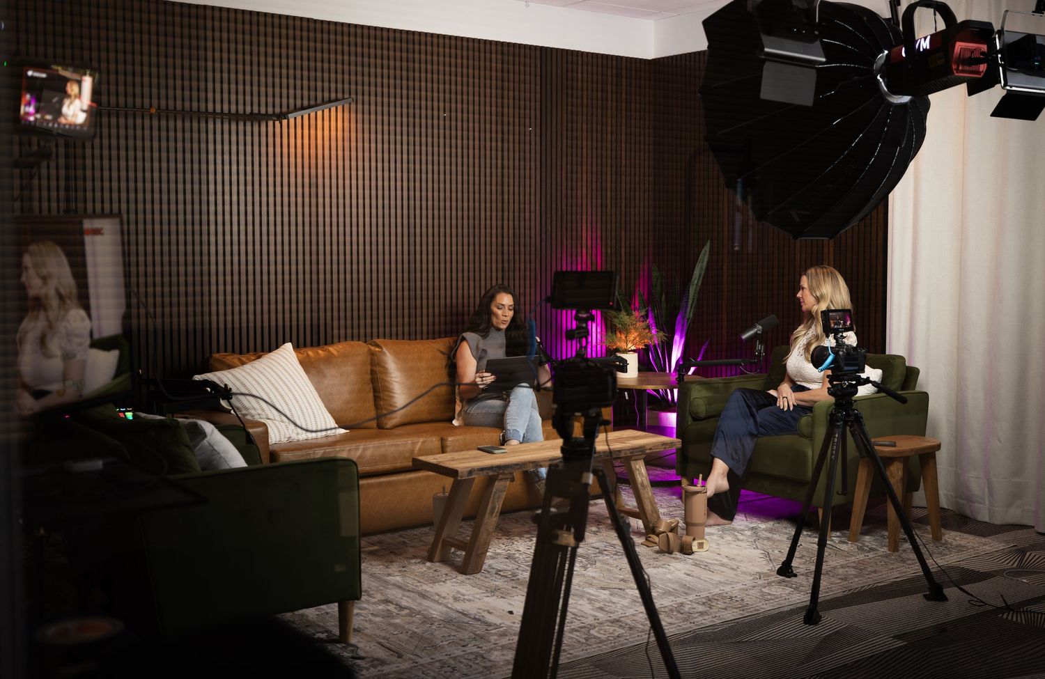Behind the scenes photo of a video production set with lighting, cameras, and a brown leather couch in a studio space.