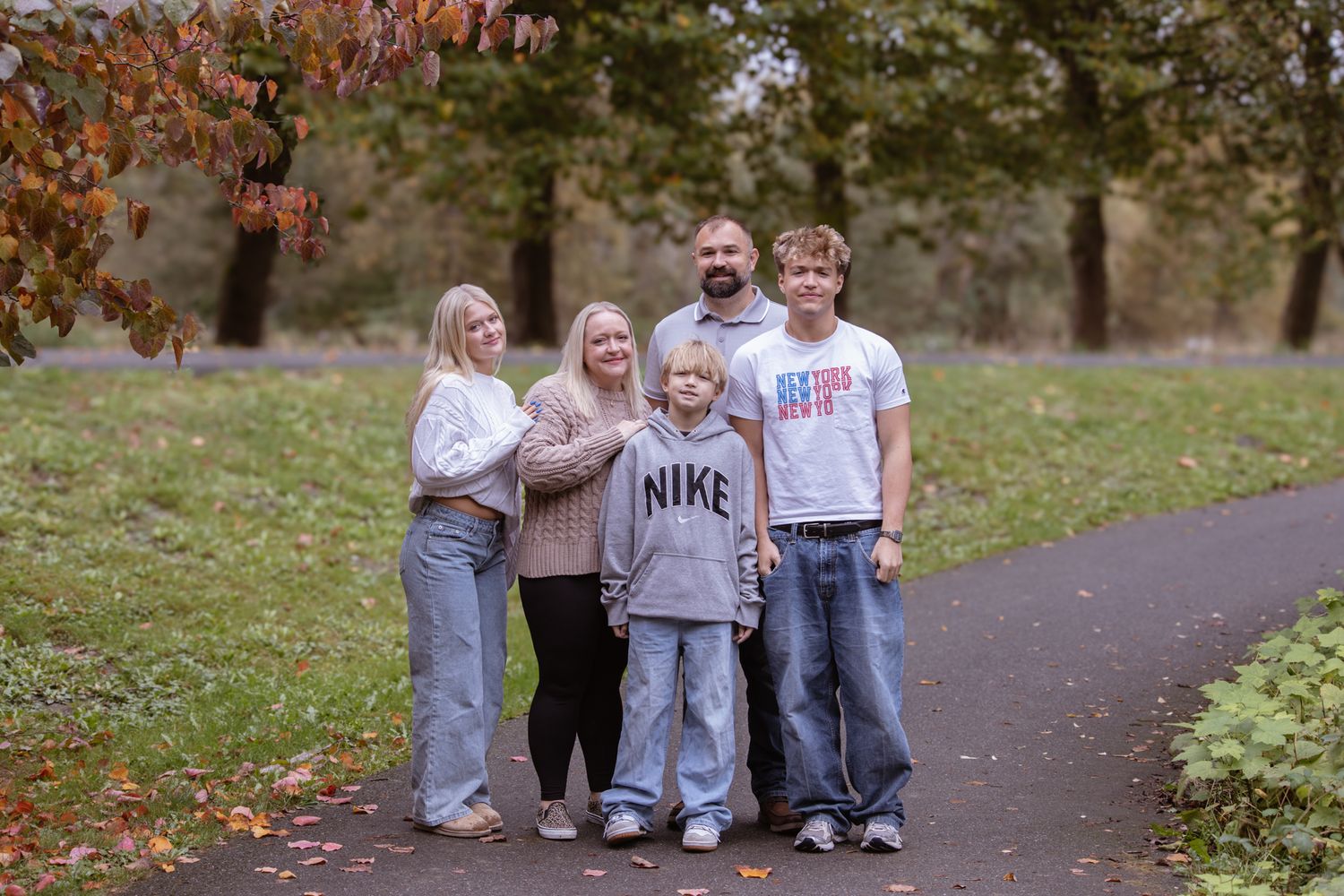 Family of five posing on a park path surrounded by autumn trees with colorful foliage in the background.