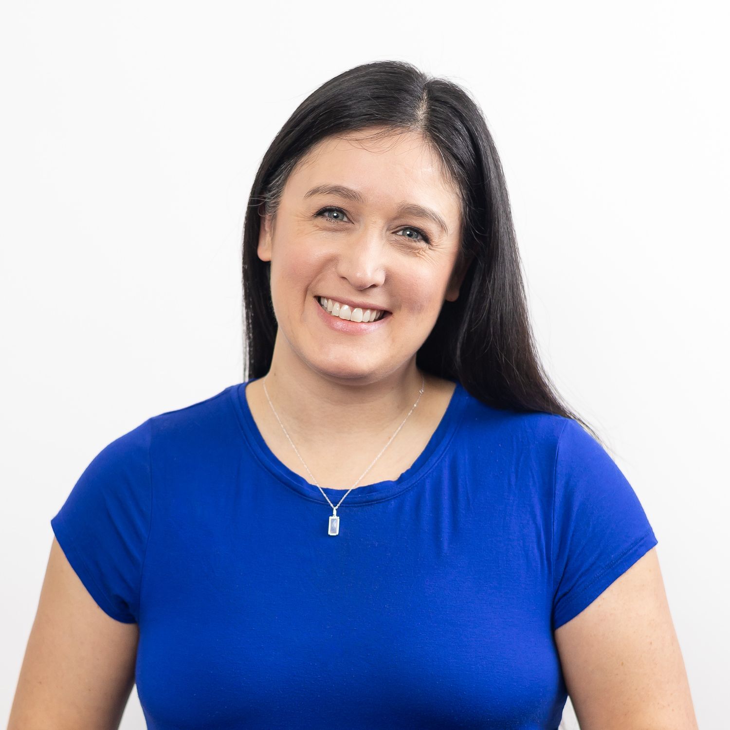 woman branding photographer headshot wearing blue shirt and moonstone necklace smiling at camera with a slight engaging head tilt Seattle WA