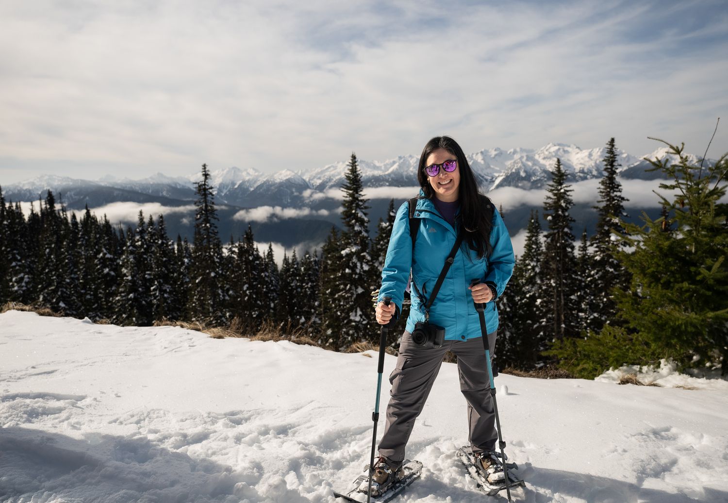 woman snowshoeing on Hurricane Ridge, WA in blue jacket and camera at hip smiling with sunglasses lifestyle adventure branding photo