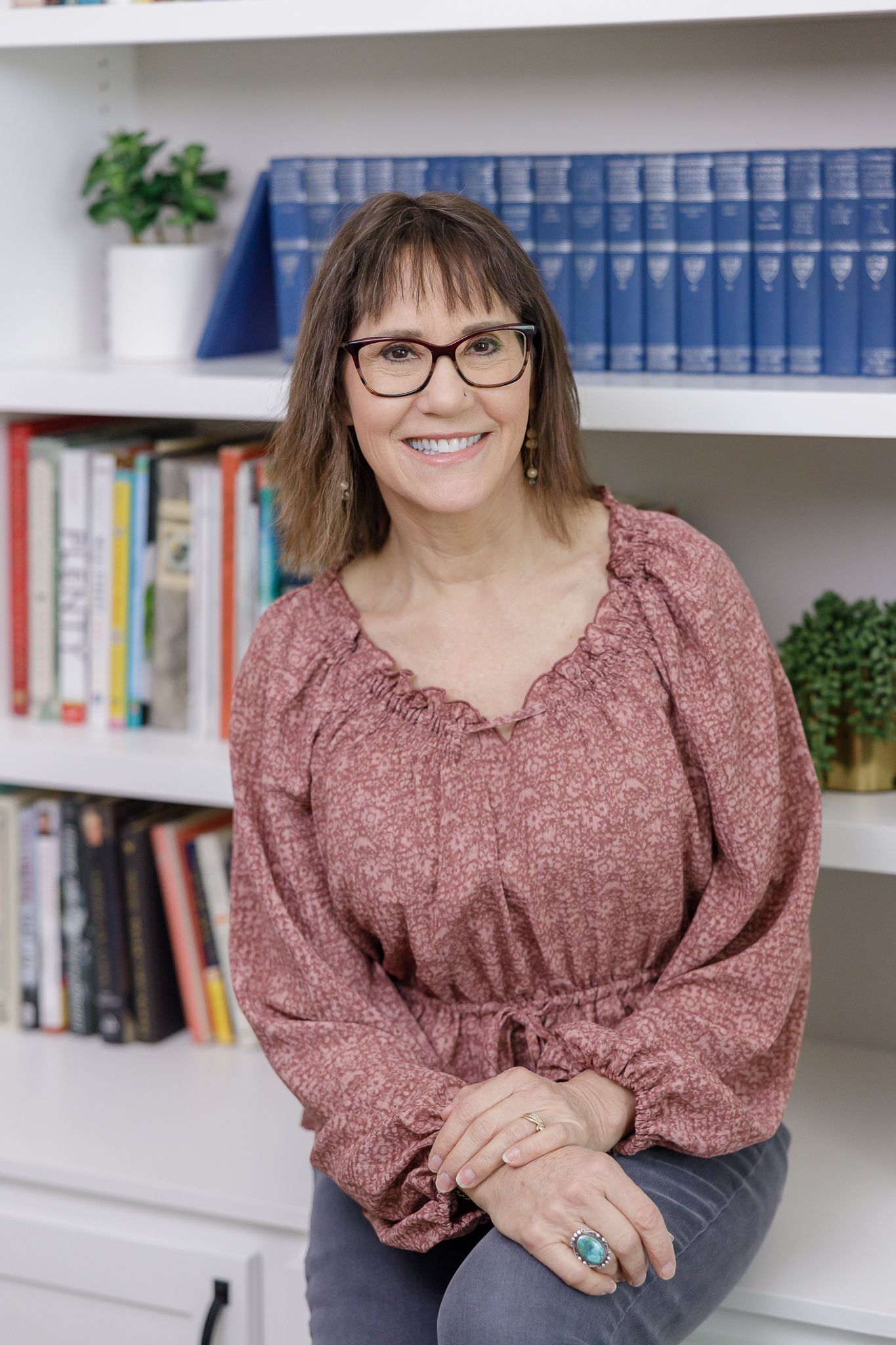 woman business owner in front of home personal library smiling at camera for lifestyle headshot wearing pink blouse in Tacoma, WA