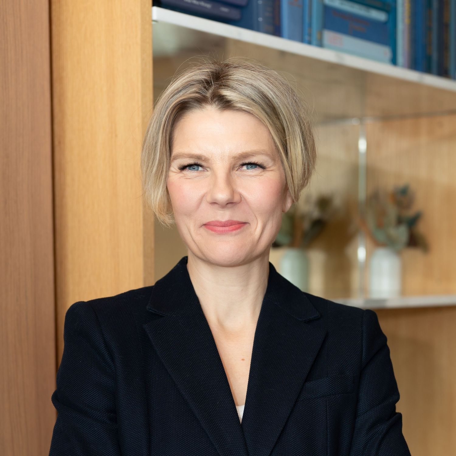 Seattle, WA based woman private neurocoach therapist headshot standing in front of office shelves smiling at camera wearing black blazer