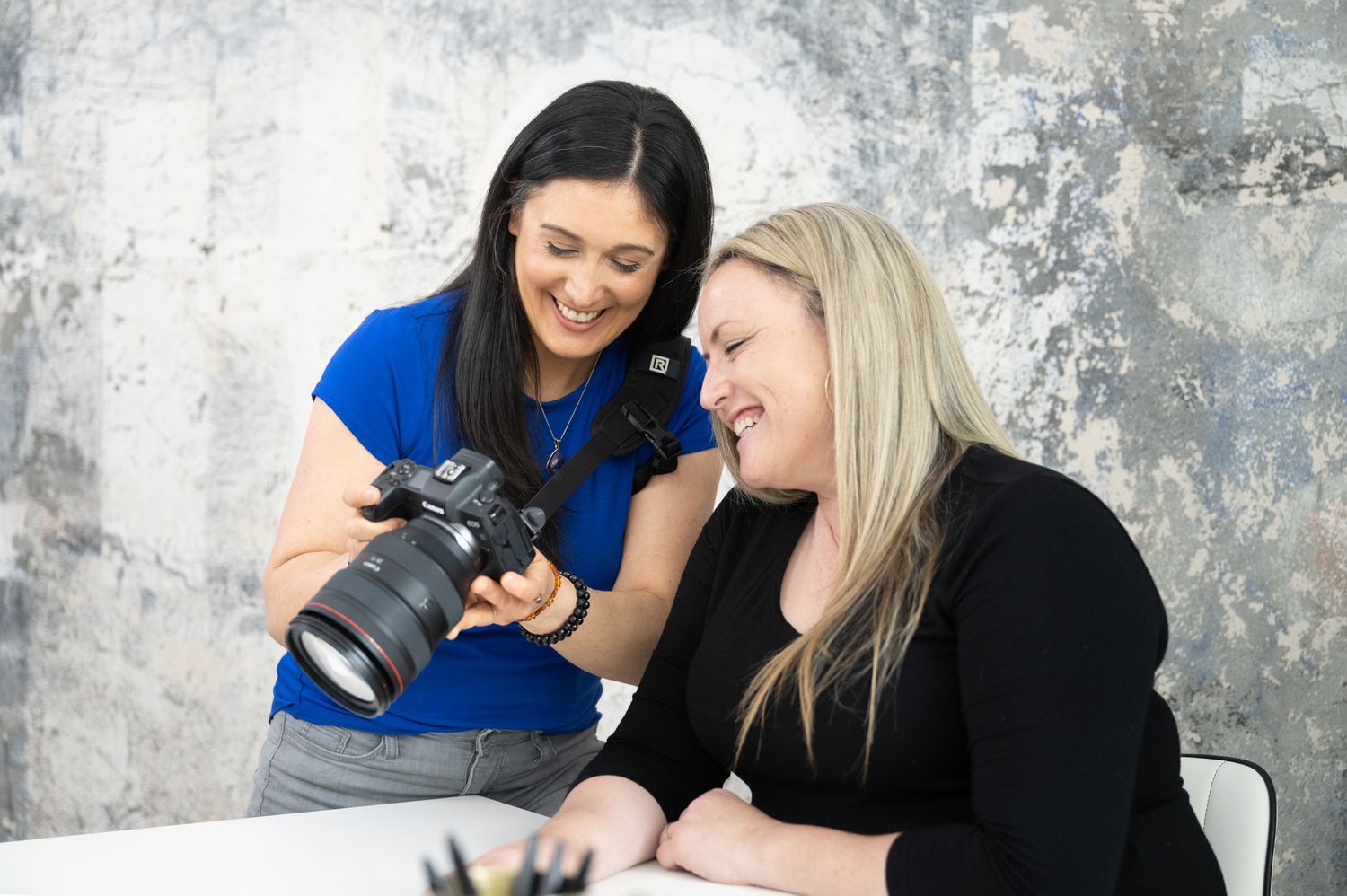 woman branding photographer showing back of camera to female client while sitting at desk both smiling in Seattle, WA studio