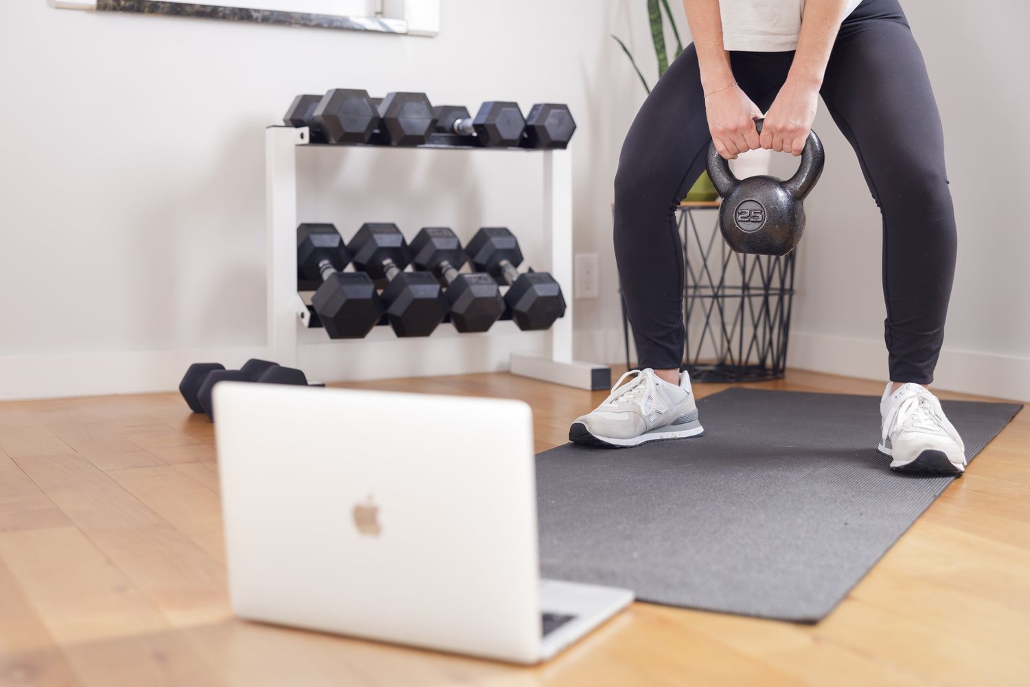 woman lifting kettlebell while looking at laptop screen for virtual class in home gym for personal trainer branding photoshoot in Seattle WA