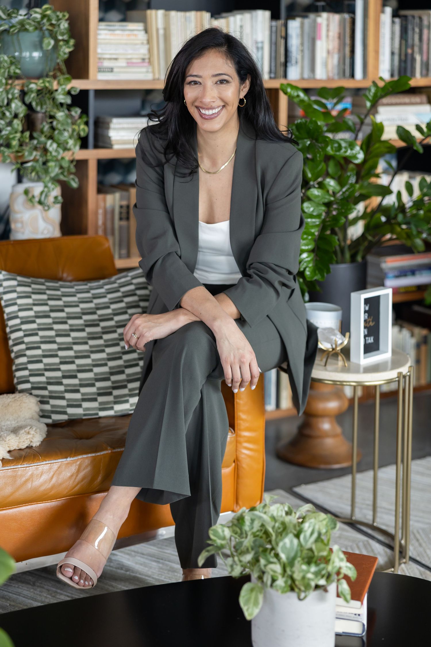 Hispanic woman sitting on couch arm in mossy green suit with white shirt smile at camera for lifestyle headshot business branding Seattle WA
