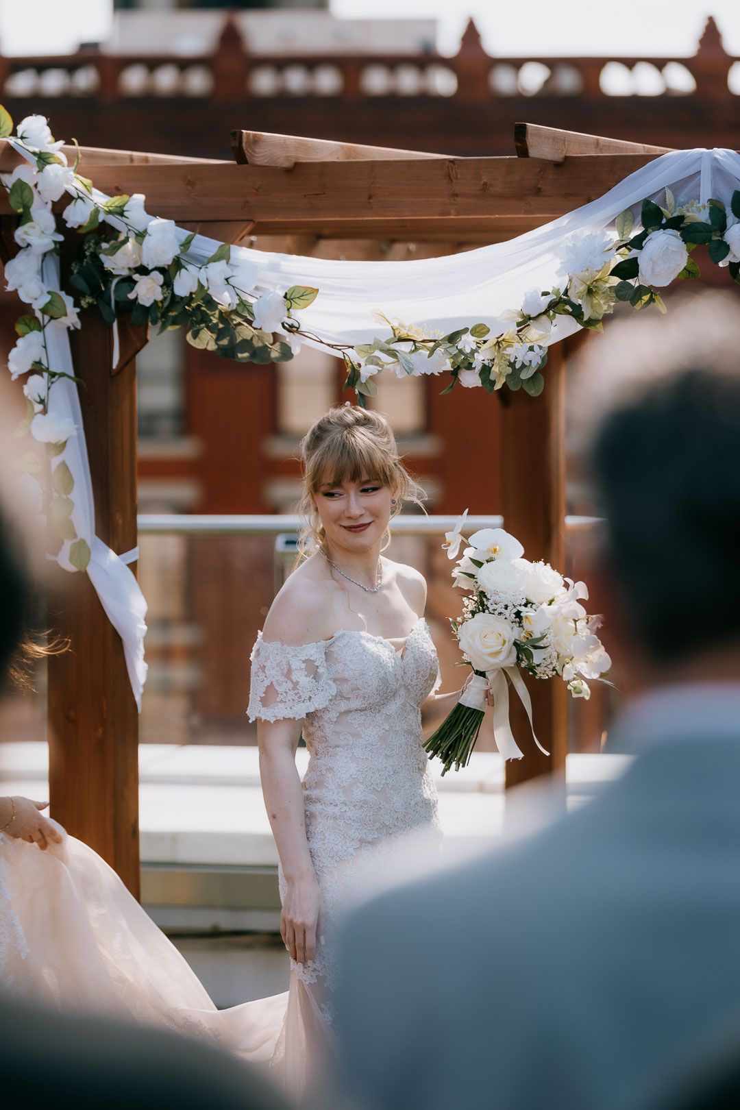 Portrait of the bride holding bouquet under floral arch during rooftop wedding ceremony by Cleveland wedding photographer.