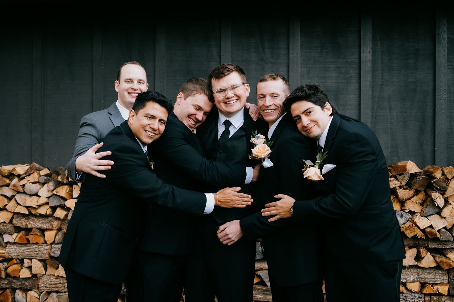 Portrait of groom surrounded by groomsmen in a joyful group hug with a natural background by Cleveland wedding photographer.