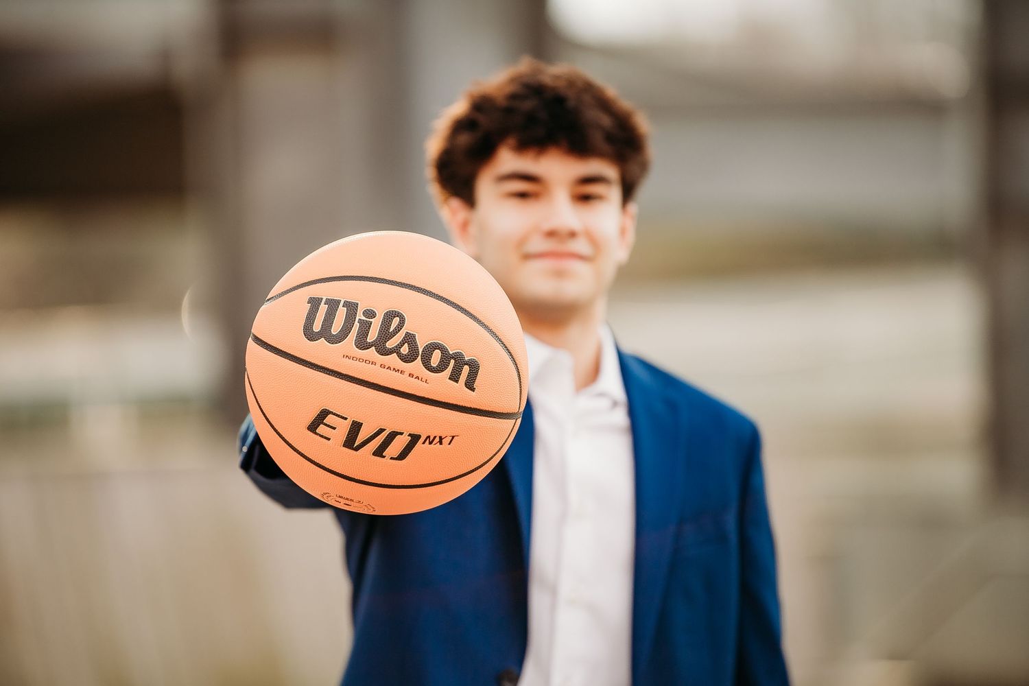 Teen boy in blue suit holding a Wilson EVO basketball toward camera on outdoor court.