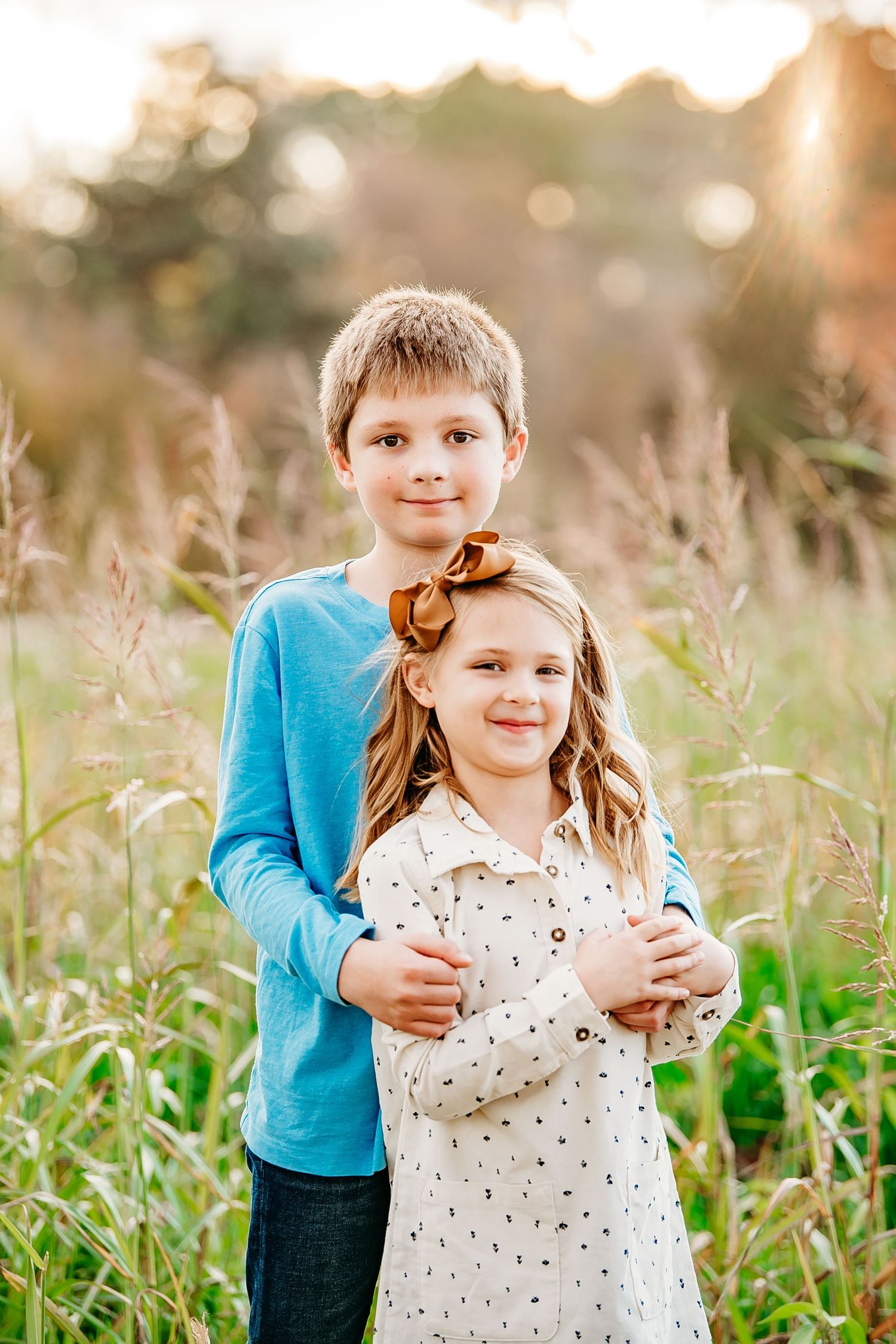 A boy in blue hugs a girl with a bow in a golden field.