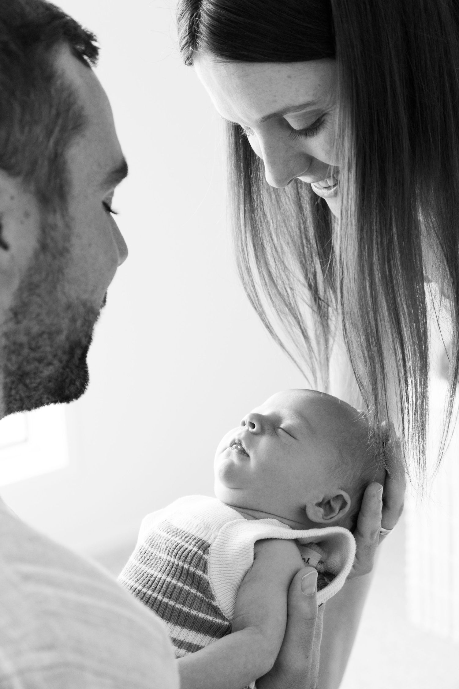 Black and white intimate photos show parents tenderly holding their newborn baby against a bright backdrop.