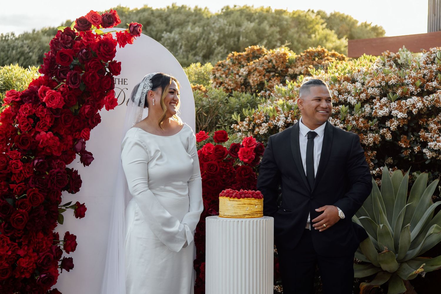 Wedding ceremony setup with vibrant red floral arrangements and elegant white decor against a lush garden backdrop.
