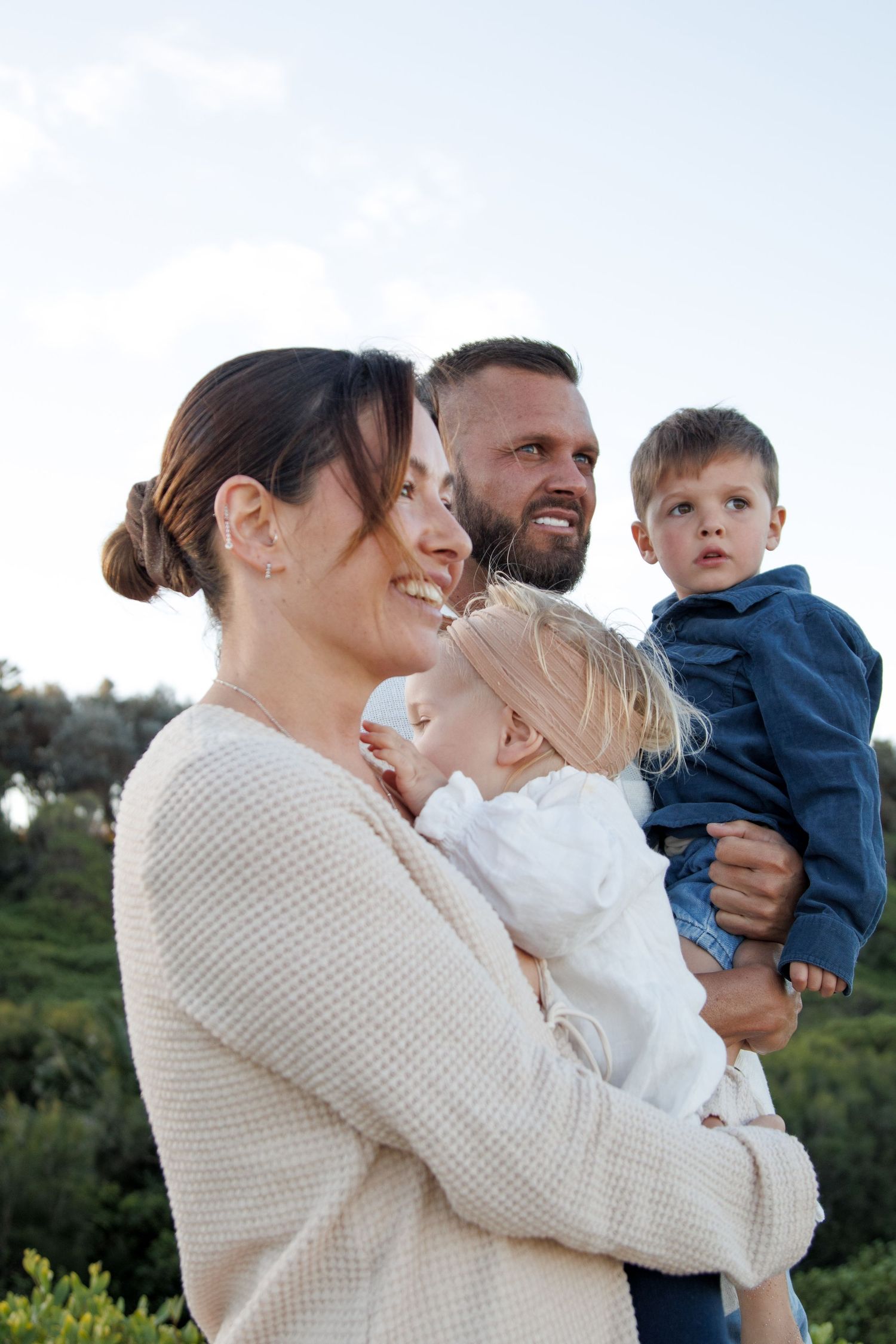 A happy family in cream colored sweaters enjoying time together outdoors against a natural landscape background.