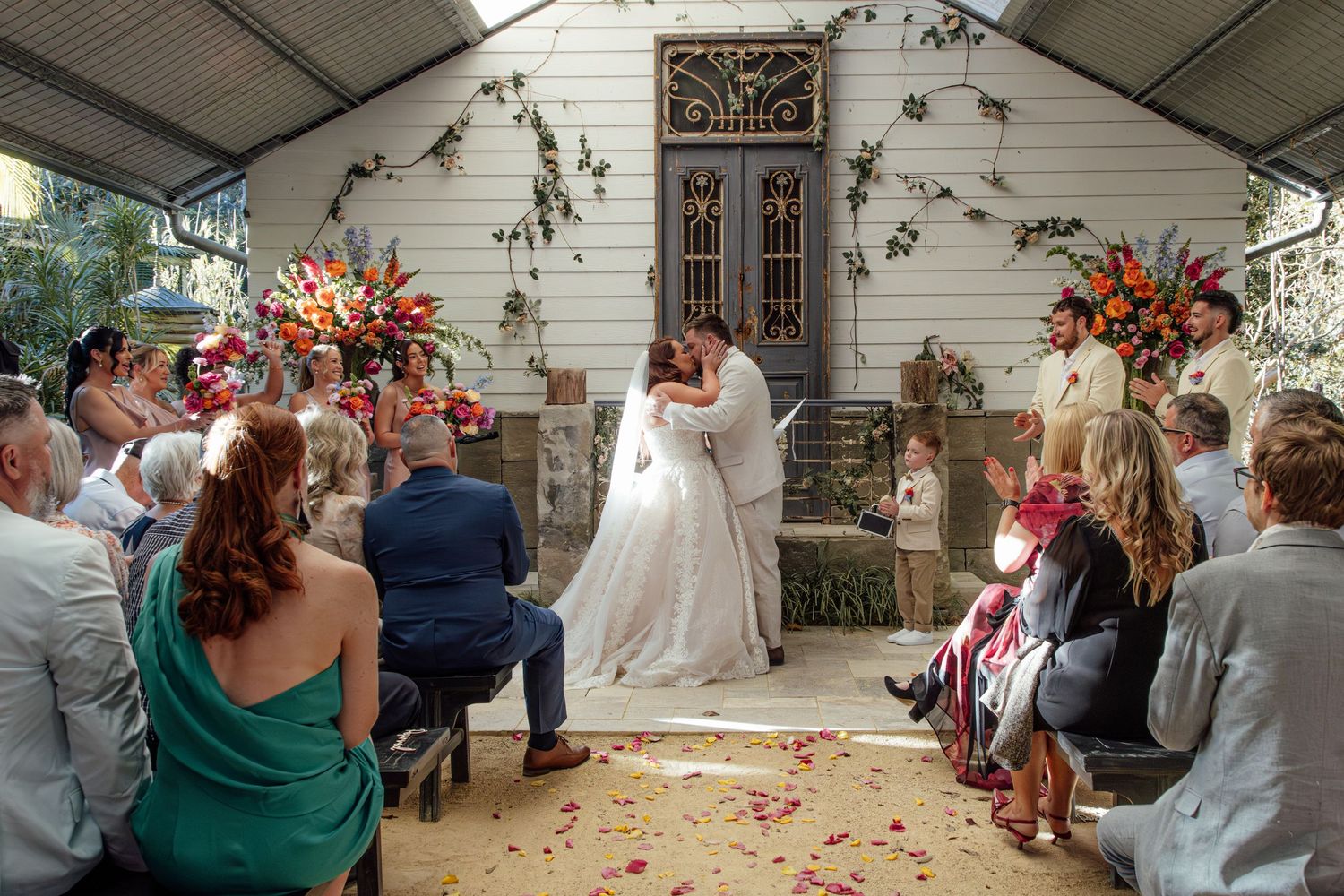 Wedding ceremony taking place in a rustic chapel with beautiful floral arrangements and rose petals scattered on the aisle.