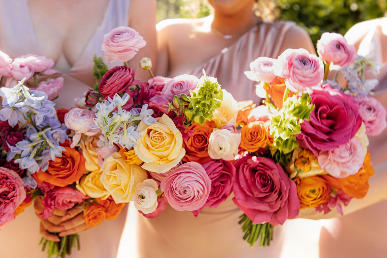 Colorful wedding bouquets featuring pink, orange, and burgundy roses with mixed greenery arranged in a row.