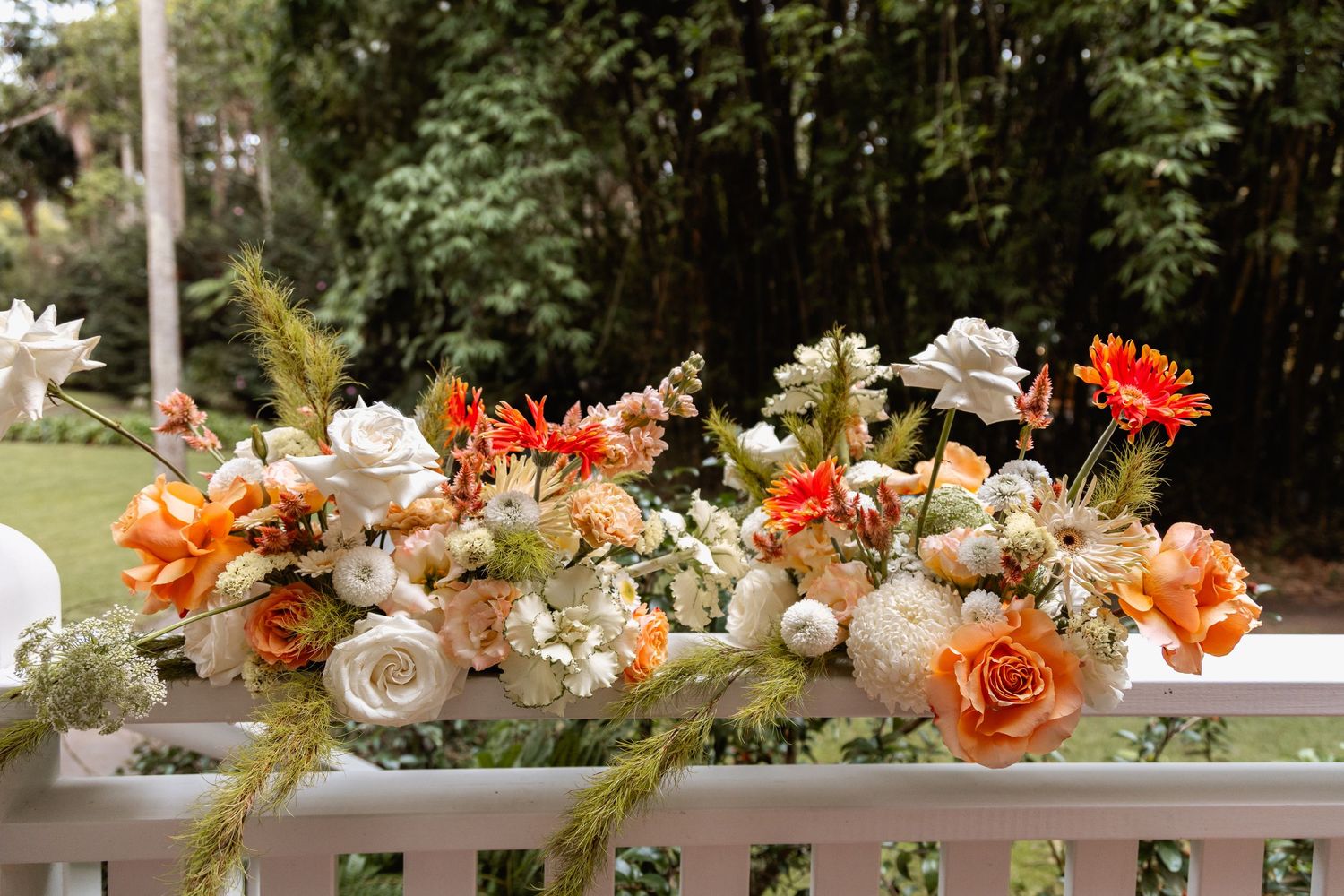 A lush floral arrangement with peach roses and white flowers adorns a white railing in an outdoor garden setting.