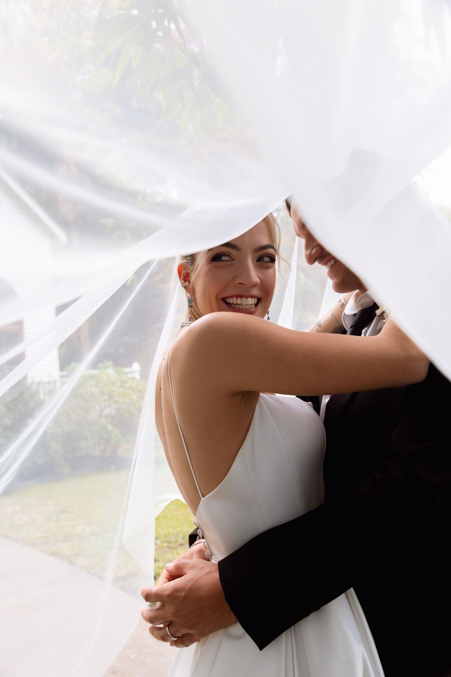 Romantic wedding moment captured with flowing white veil framing the couple's embrace.