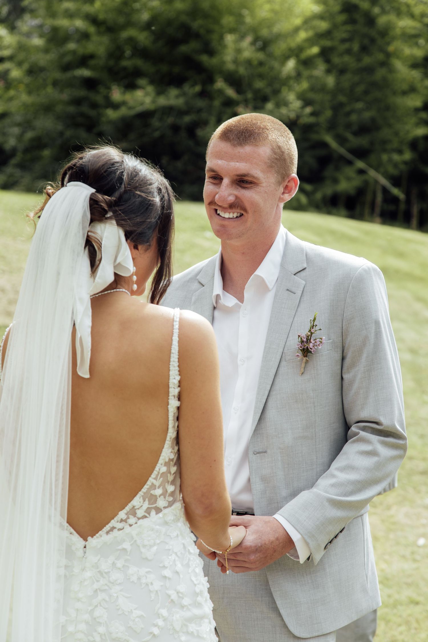 Newlyweds share a joyful moment outdoors during their wedding ceremony, with the bride in a backless dress and flowing veil.
