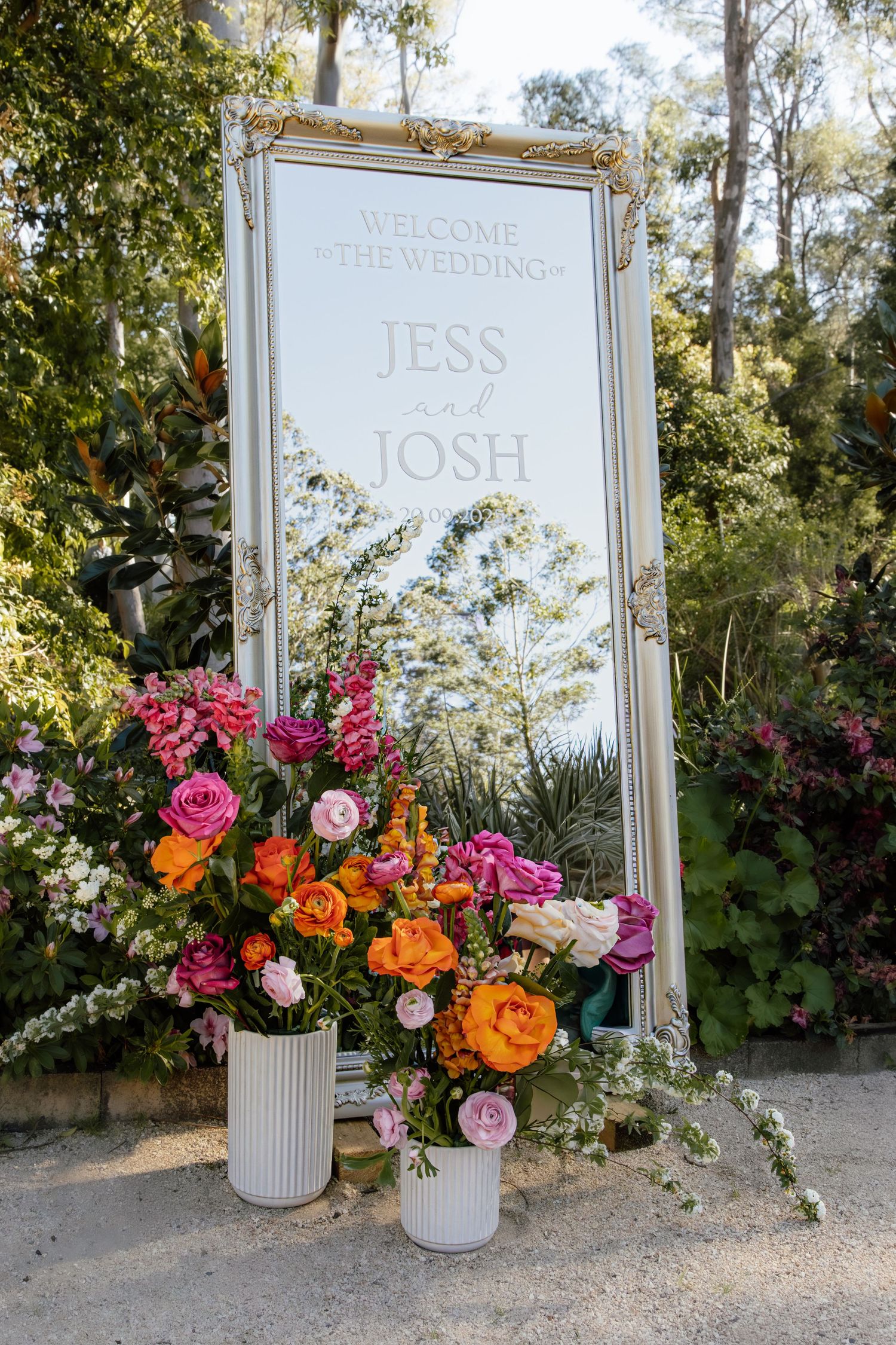 Elegant white-framed wedding welcome signs with vibrant pink, orange and white floral arrangements in modern vases.
