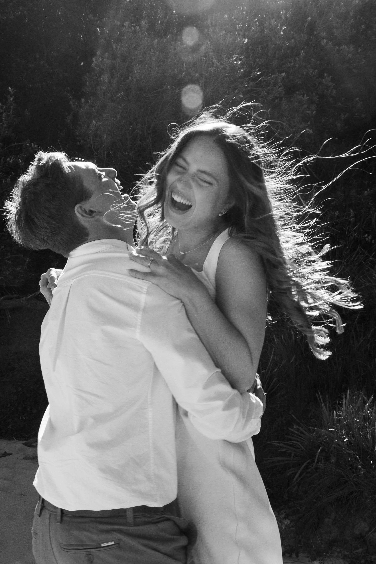 Two figures share a romantic black and white moment as the wind blows their hair during an outdoor photoshoot.