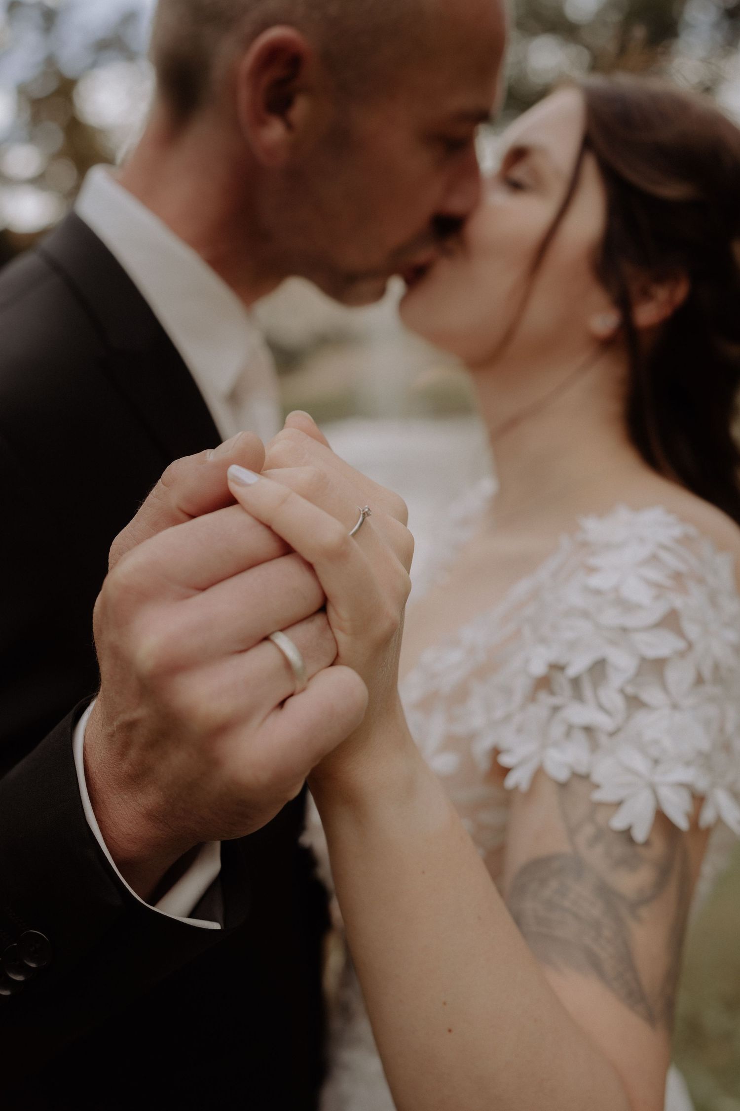 A tender moment showing intertwined hands with wedding rings against formal attire.