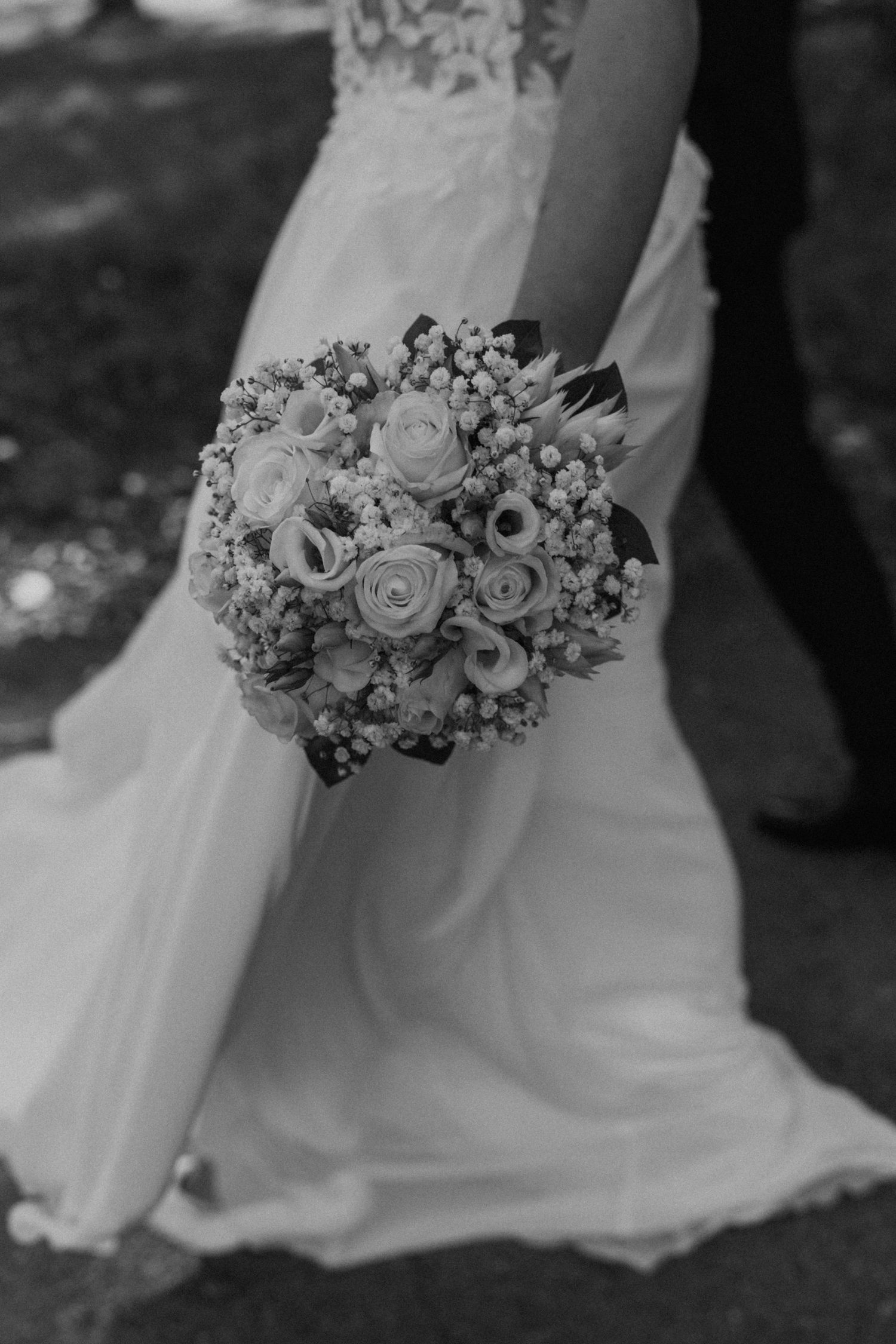 Black and white photo of a bridal bouquet with roses and baby's breath against a flowing wedding dress.