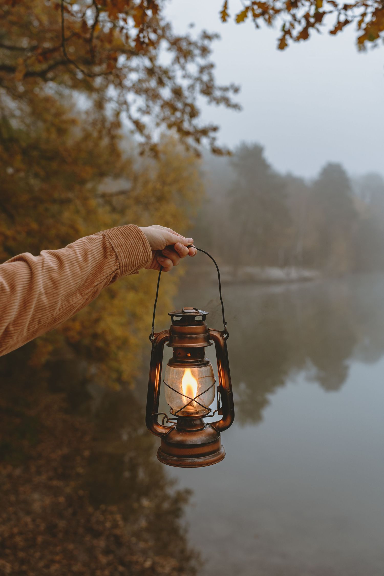 Glowing oil lantern held against foggy lake during fall season.