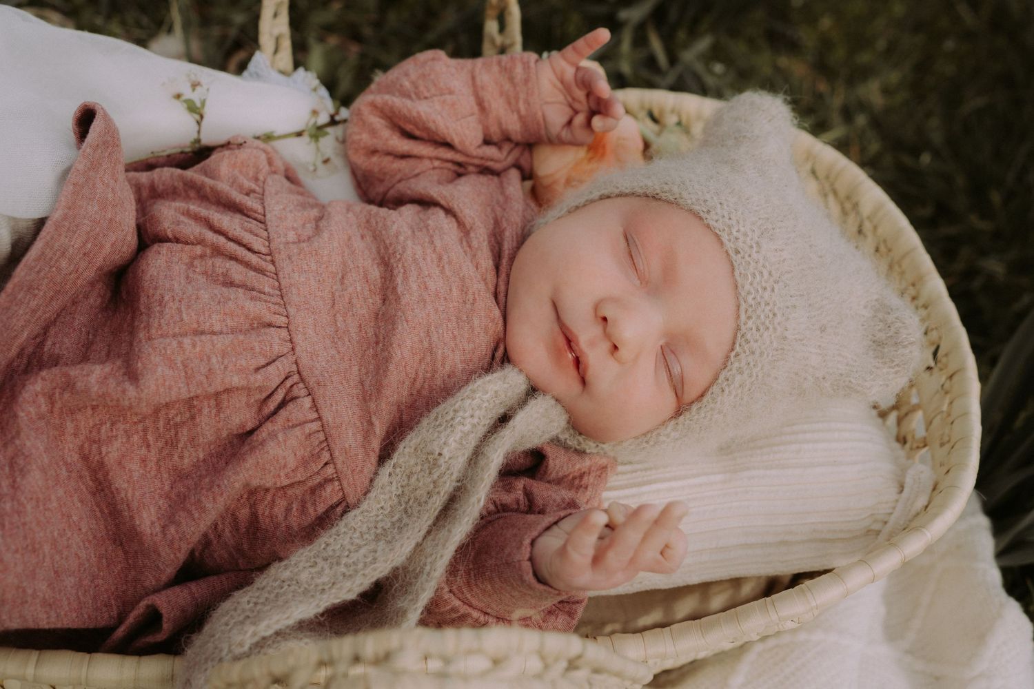 Baby in soft pink outfit rests in cozy white bedding.