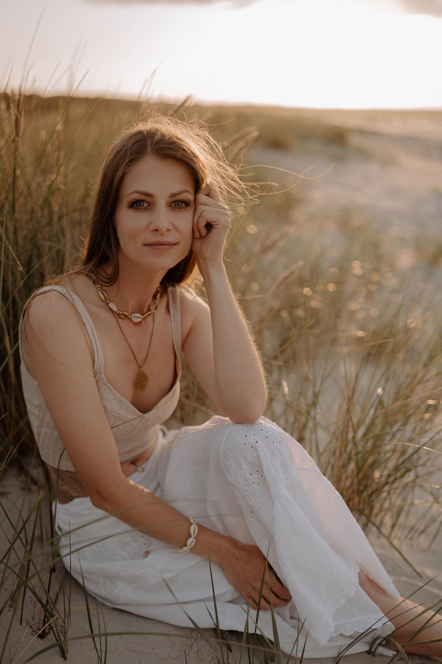 Romantic portrait in white dress among coastal dunes at golden hour.
