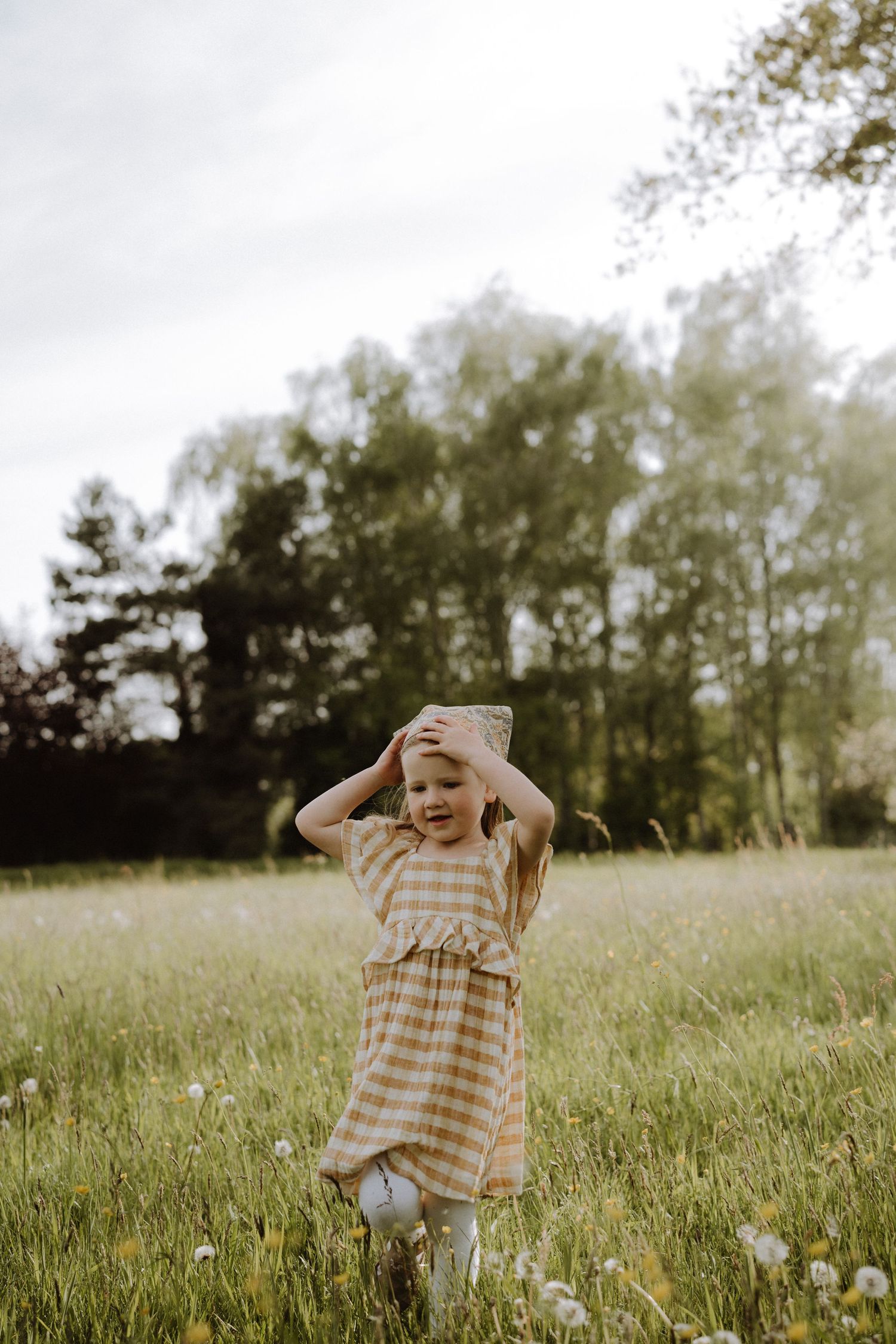 Someone running through a wildflower meadow wearing a checkered dress on a cloudy day.