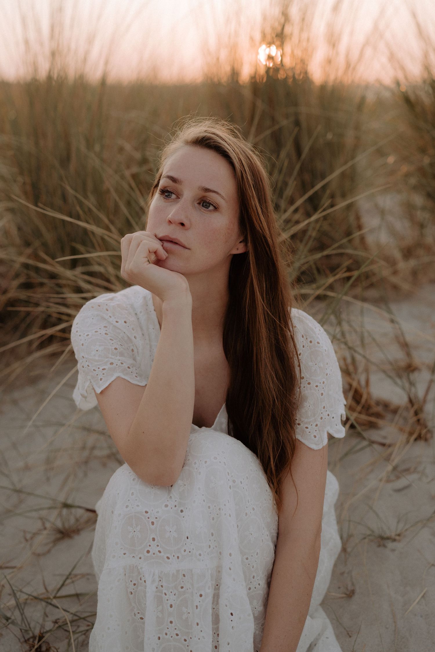 Dreamy portrait in white eyelet dress against sunset in beach grass.