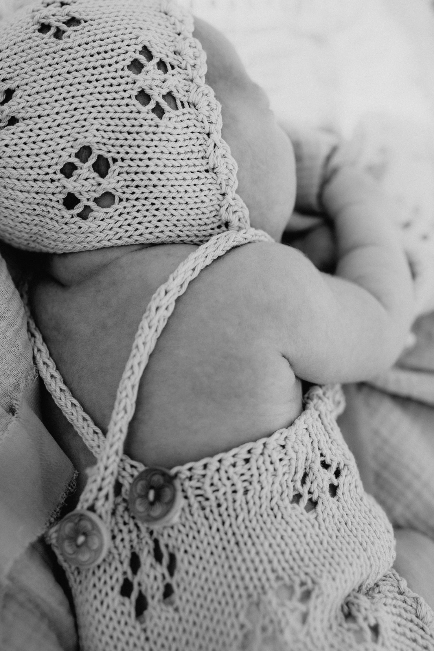 A newborn baby wearing delicate white knit lace clothing.
