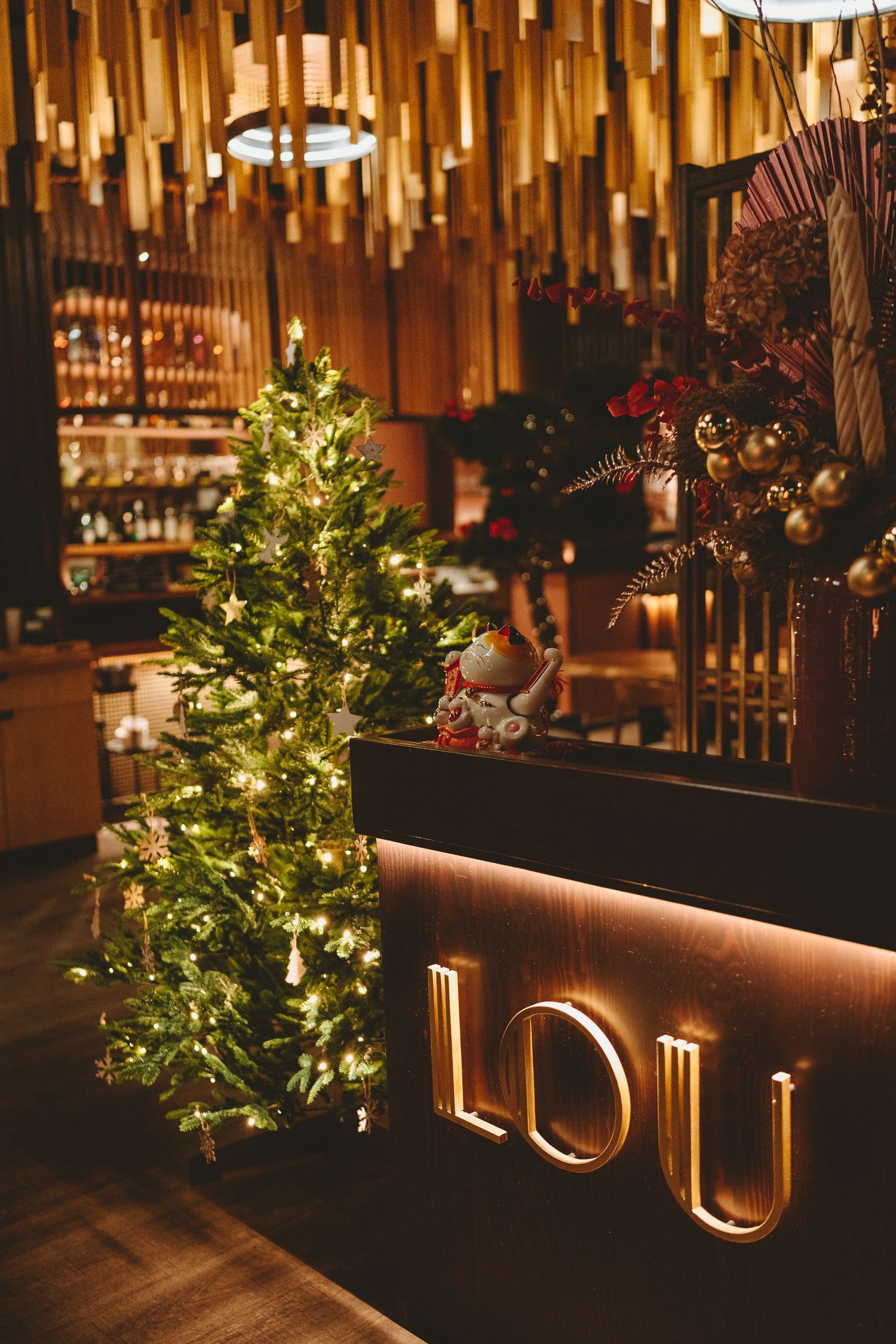 Cozy restaurant ambiance with lit Christmas tree and golden LOU signage against warm lighting.