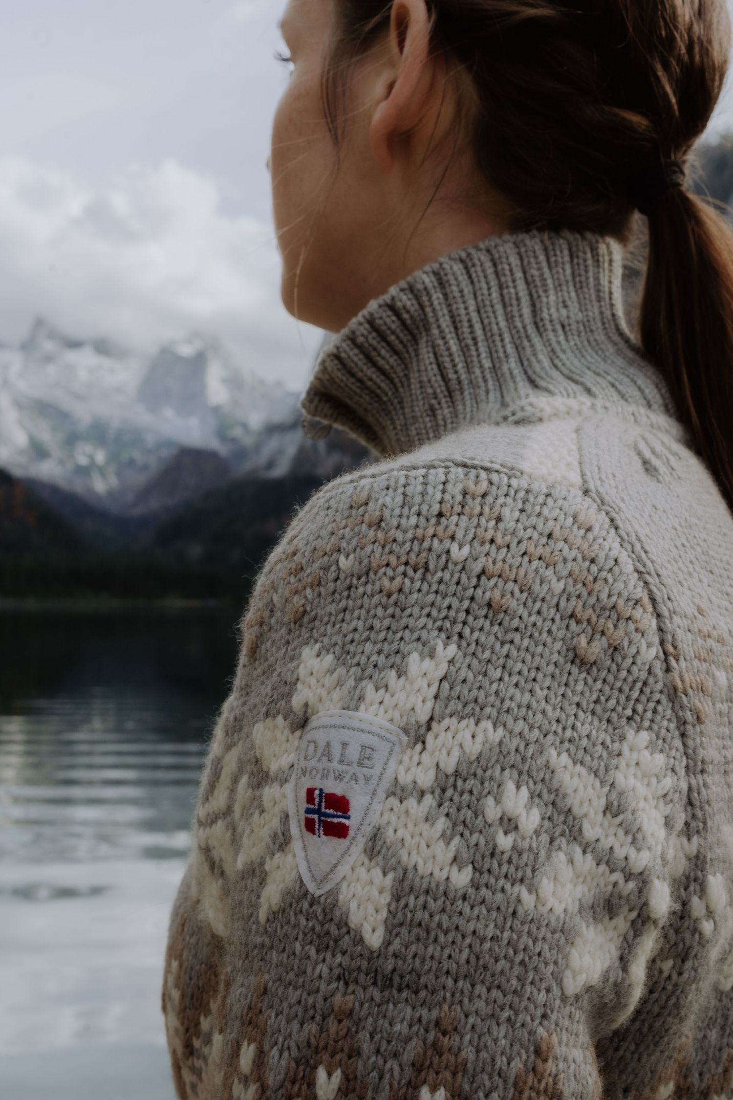 Close-up of Norwegian flag patch on knit sweater with mountain lake backdrop.