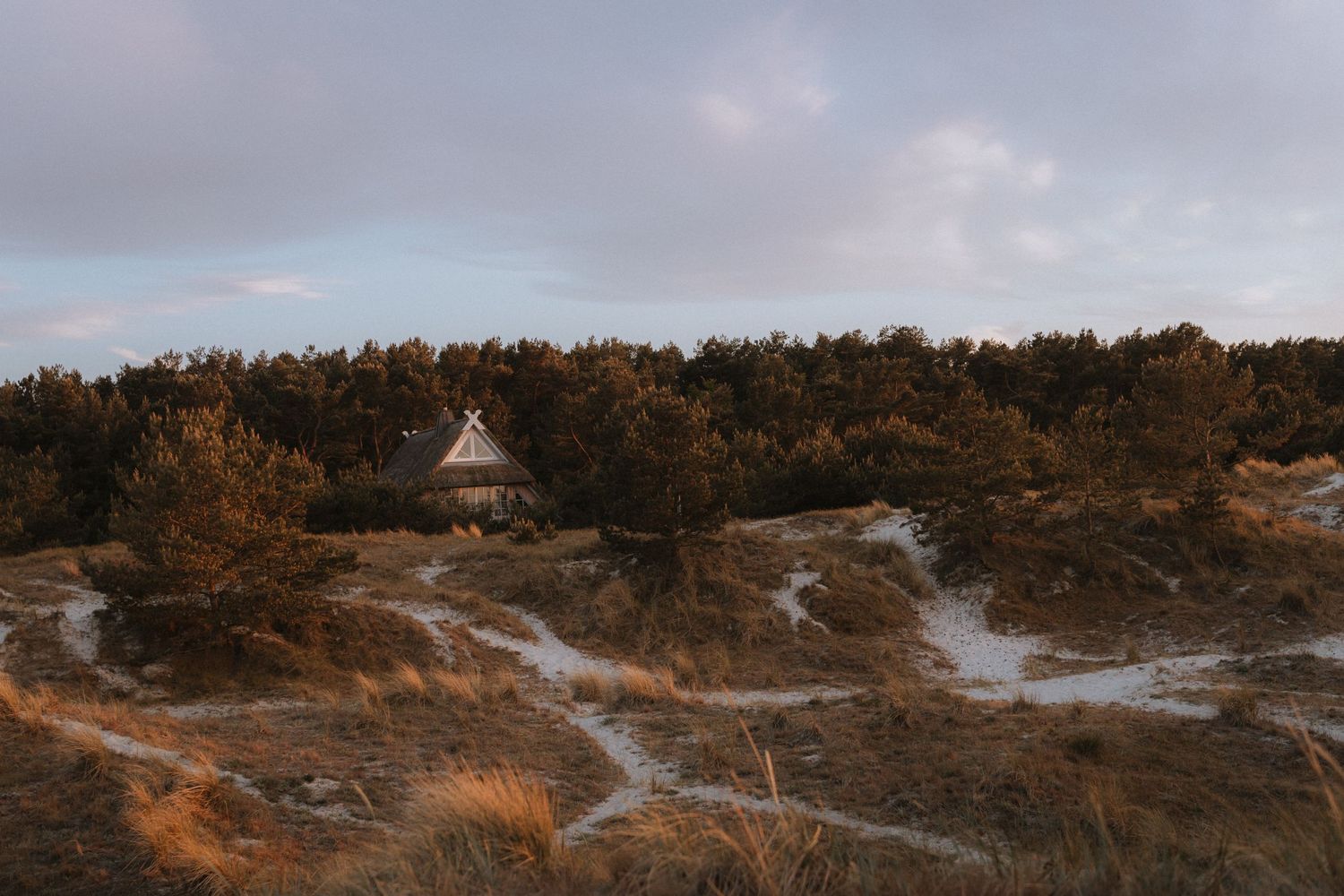 Small wooden structure sits atop golden hillside with winding trails during sunset.