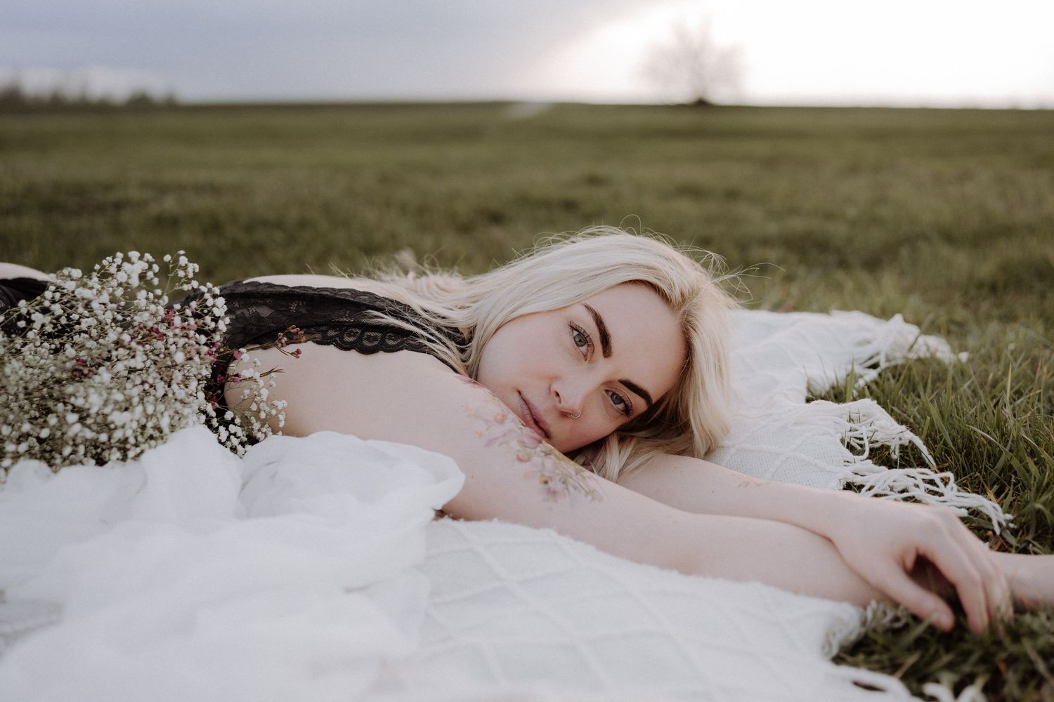 A woman in white lying in a field with baby's breath flowers scattered around her.