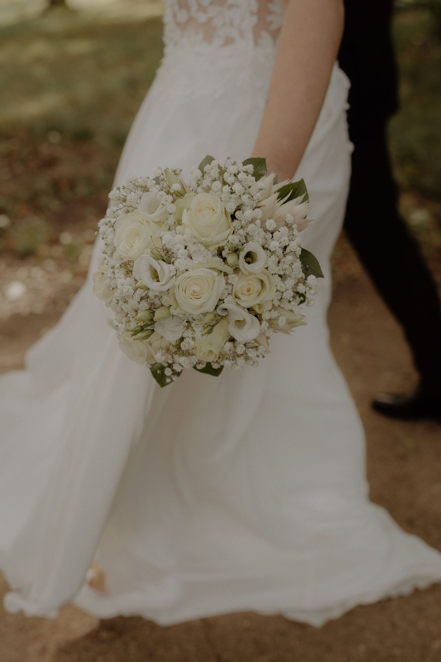 A close-up of an elegant white bridal bouquet with roses and baby's breath against a flowing wedding dress.