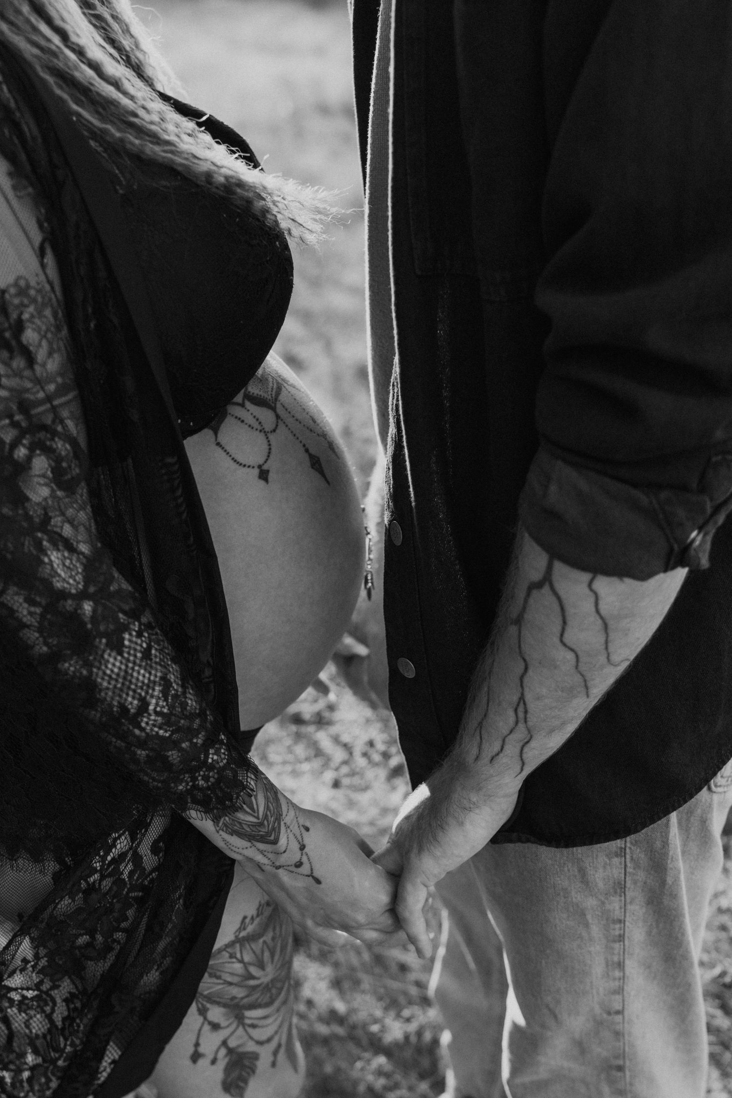 Black and white close-up of two people holding hands, showing matching tattoos.