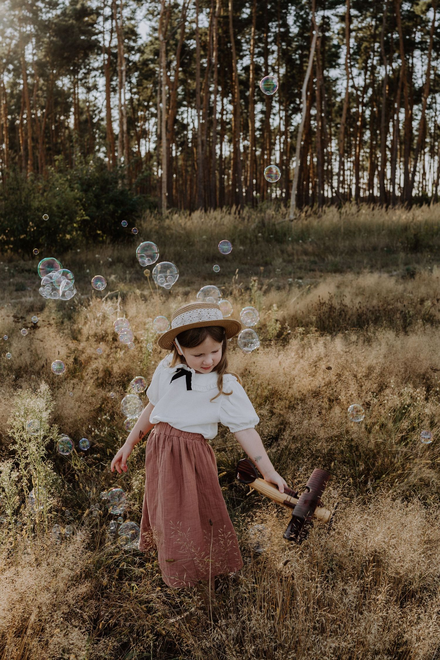 Young child playing with bubbles in a forest clearing while wearing a vintage-style outfit.