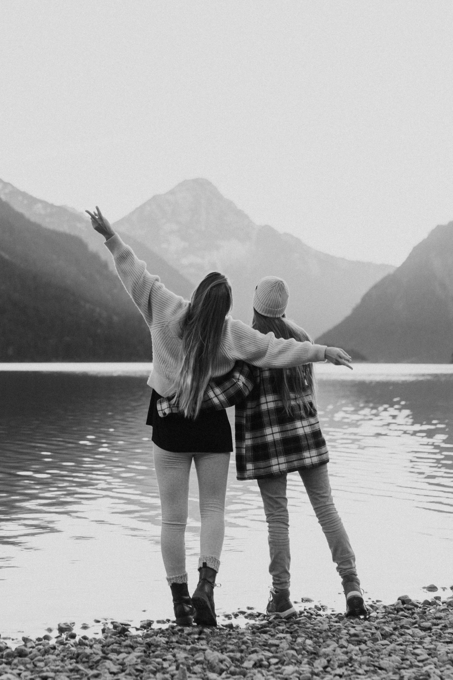Two friends sharing a joyful moment by a mountain lake with arms raised in celebration.