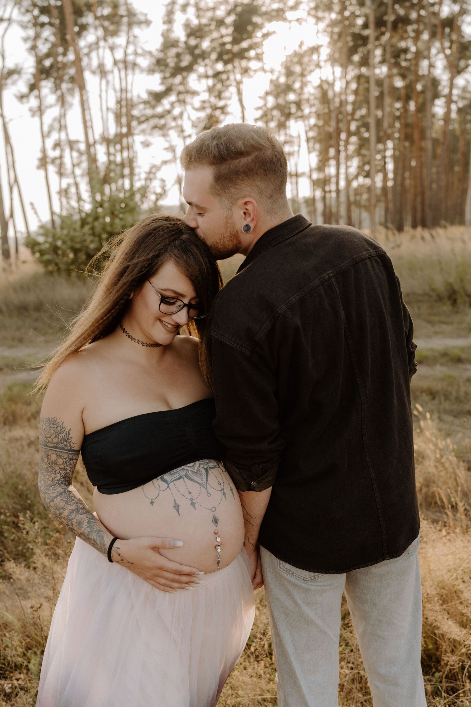 Intimate maternity portrait in a forest setting with soft golden light.
